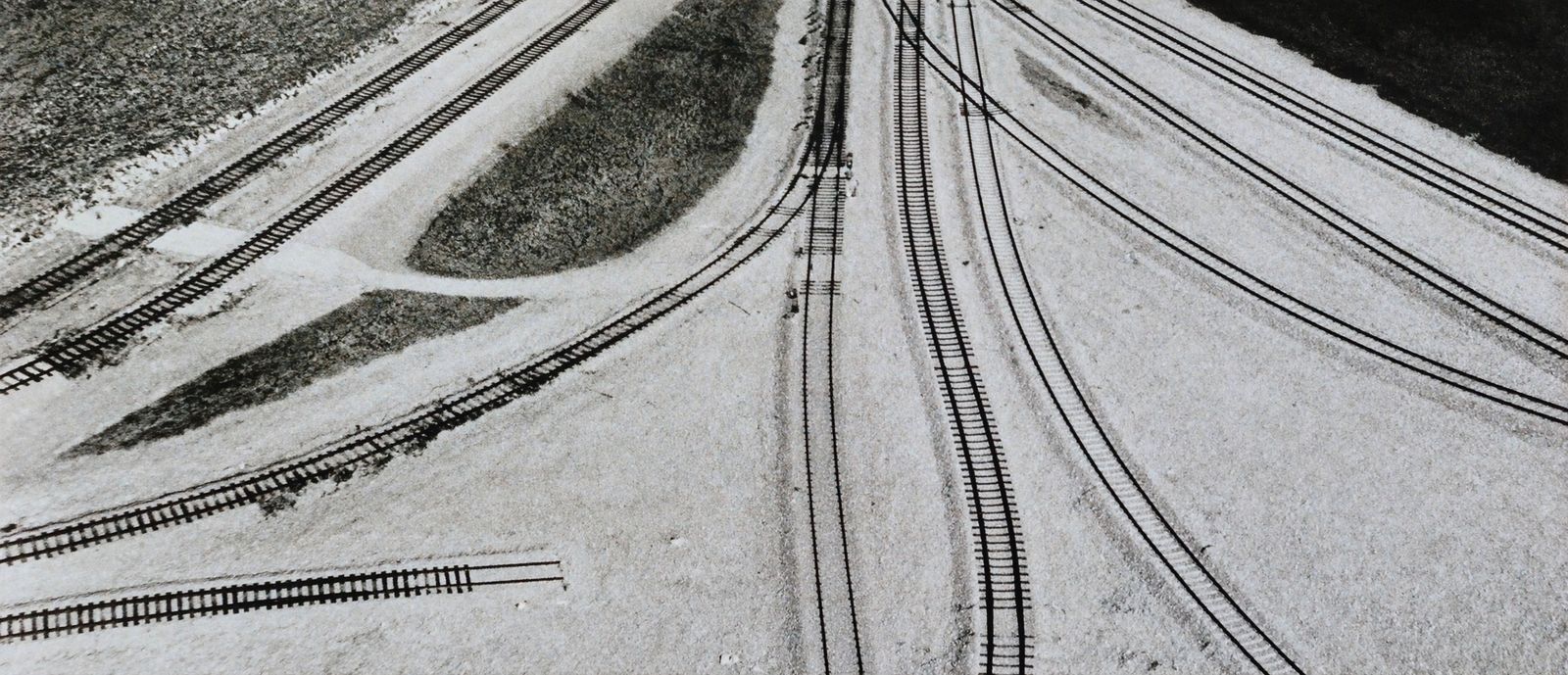 Seen from above, railway tracks fan out from one point across pale ground.