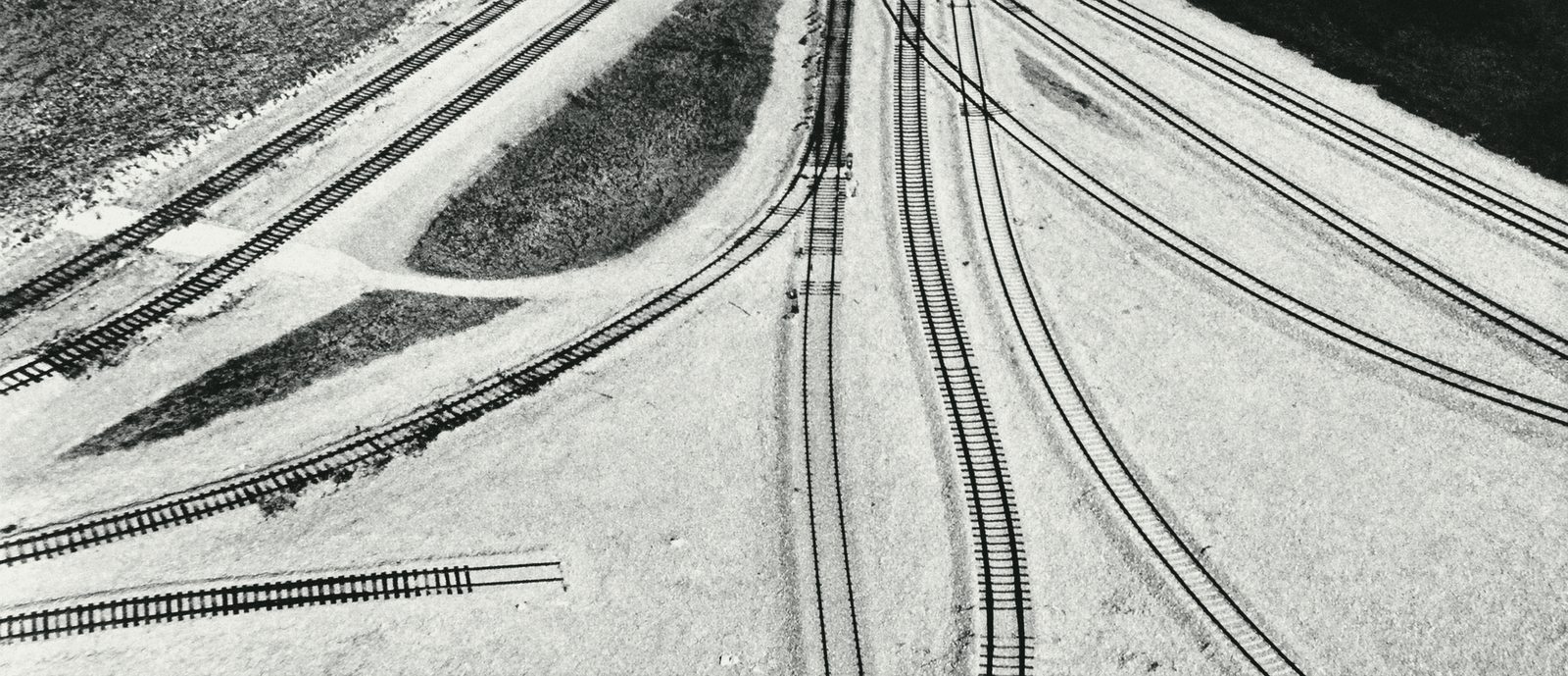 Seen from above, railway tracks fan out from one point across pale ground.