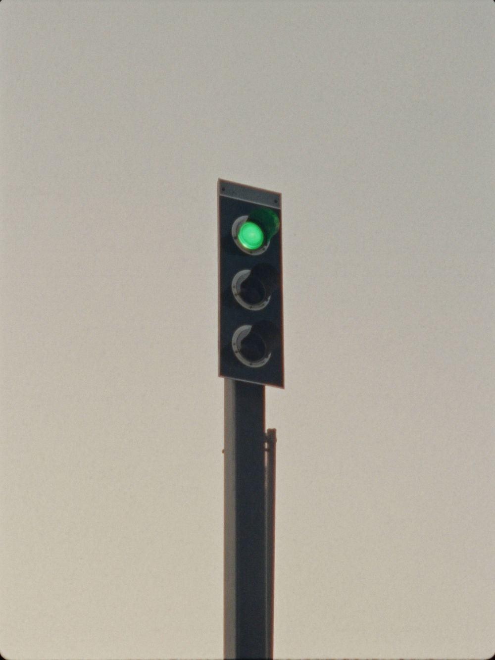 A railway signal on a tall post against a pale sky, its green lamp lit.